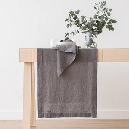 A long, rectangular linen runner in a steel grey color with a stone-washed finish. The runner is suitable for use on a table or other flat surface, and is available in multiple size options.
