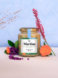  A jar of spring honey with a green and white label. The honey has a vibrant golden color and is surrounded by colorful flowers, suggesting a natural, artisanal product.