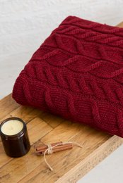 Red cable-knit throw blanket made of soft merino wool, featuring a cozy and textured design.