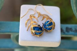 Nature-inspired gold-plated brass earrings with Murano glass in green and blue colors, featuring a dangle and leverback style.