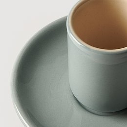Ceramic coffee cup in a muted blue color, with a matching saucer. The cup has a simple, minimalist design.