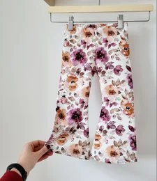 Flared kids pants with a floral print pattern in shades of brown, beige, and white. The pants have a wide leg silhouette and are available in sizes 74/80 through 122/128.