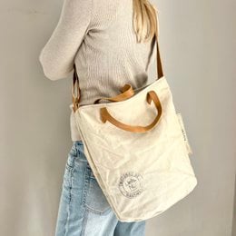 Vintage-inspired beige canvas shoulder bag with leather handles and a simple, minimalist design.