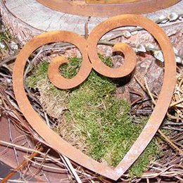 A decorative metal heart-shaped sculpture with a swirling design, suitable for hanging or staking in a garden. The heart-shaped sculpture is made of a warm, rustic-looking metal material and features a swirling, curving design. It appears to be intended as a decorative garden accent or Mother's Day gift.