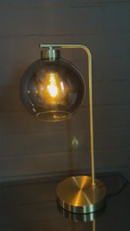A gold-colored table lamp with a round glass shade, providing warm, ambient lighting.