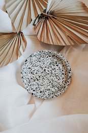  Round tray, white speckled ceramic, natural woven palm leaf decorative accents, minimalist style.
