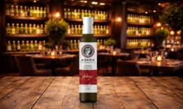  Infused olive oil with garlic and chili flavors, presented in a glass bottle on a wooden table against a blurred background of shelves filled with liquor bottles.