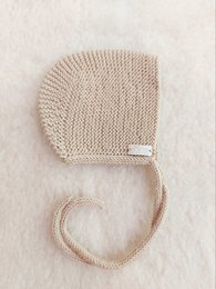 A cozy, sand-colored merino wool bonnet hat for babies. The hat features a simple, minimalist design with a soft, knitted texture.
