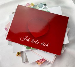 A red gift card with the text "Ich liebe dich" (I love you) and a heart-shaped pendant on a gold chain.