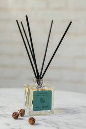 Green glass bottle with wooden cap and black reed diffuser sticks. Rectangular cardboard box with green label "The New Fragrance Collection".