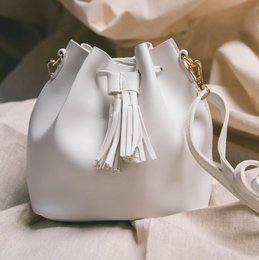 White leather bucket bag with tassel detail and adjustable strap.