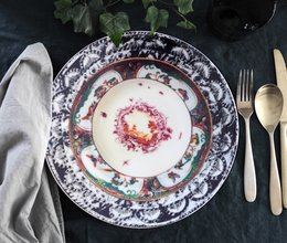 A round, white ceramic plate with a floral design in the center, surrounded by a patterned border. The plate appears to be part of a dining set or tableware collection.