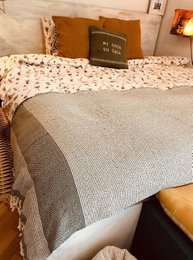 A cozy, textured bedspread in neutral tones with a patterned accent pillow. The bedspread appears to be made of a soft, woven material and is available in a variety of colors to complement different bedroom styles.