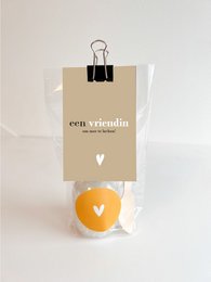 Gift bag of bath salts in a neutral-colored paper bag with a heart-shaped bath bomb and a wooden spoon.