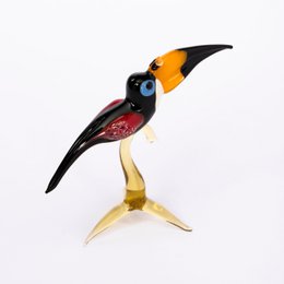 Glass toucan statue with a black body, yellow beak, and red accents perched on a branch.