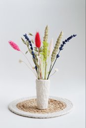 A ceramic vase holding a bouquet of colorful dried flowers, including red, yellow, and green floral elements. The vase has a textured, earthy appearance.