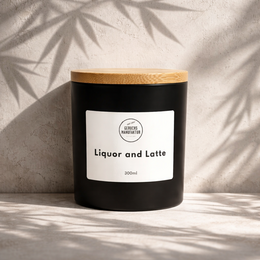 A tall, round black candle with a gold lid, labeled "Liquor and Latte". The candle has a rich, dark color and appears to be a premium scented candle.