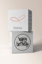A white gift cube with the text "HAPPY BIRTHDAY" printed on it, along with a round gift box with the text "happy birthday" printed on it.