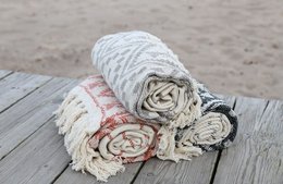 Soft, cozy beach throw in a variety of colors including red, black, and grey. Made from durable, woven material with a textured pattern.