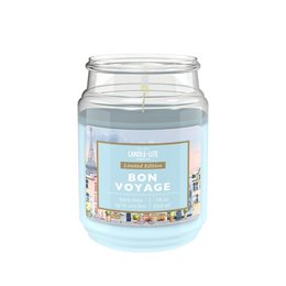  A large, round, clear glass candle jar with a blue label that reads "Bon Voyage". The candle appears to be a light blue or white color. The label features illustrations of various travel-related items like a suitcase, airplane, and compass.