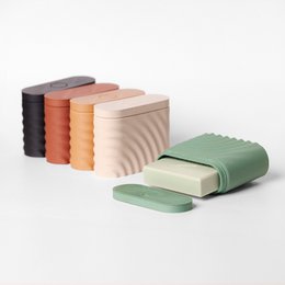 Rectangular travel soap case in various colors including ebony, cedar, birch, red, and green. The case features a ribbed texture and includes a matching soap bar.