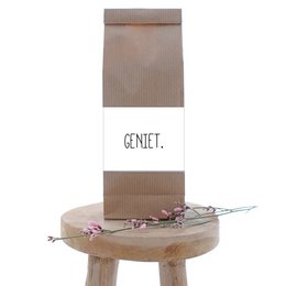 A brown paper bag with the text "GENIET." printed on it, containing a wooden stool and some decorative items.