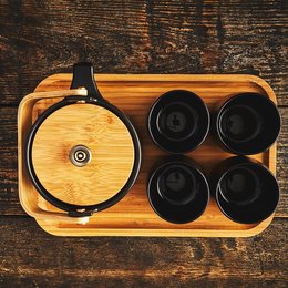 Black ceramic tea set with round teapot and 4 cups on wooden tray