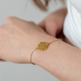 Gold-toned bracelet with a circular charm featuring a repeating flower of life pattern. Delicate chain design.