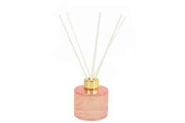 A tall, round pink reed diffuser with a gold cap and white reeds. The diffuser is part of a set that includes matching pink candles.
