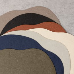 Beige leather placemat and coaster set with round shape and textured surface. Includes a 36 x 29 cm table mat and a 13 x 12 cm coaster.