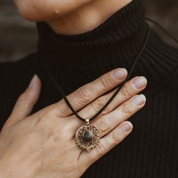 Sunshine necklace charm with a round, ornate pendant featuring a central stone. The pendant has a vintage, filigree-like design in a gold-toned metal.