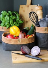 A round, tall black paper bag with a leather edge and a waterproof biodegradable liner. The bag is available in various sizes, including Ø13x H13cm, Ø15 x H15cm, Ø20 x H20cm, Ø20 x H10 cm, and Ø25 x H10 cm.