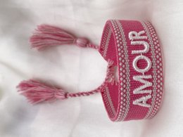 Vibrant pink charm bracelets with tassels and text designs. Includes 'Amour' and 'Good Vibes' styles in a variety of pink and red hues.