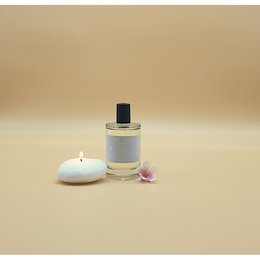 Elegant glass perfume bottle with a white candle and pink flower petals. The perfume is described as a floral, feminine scent.