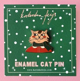 A seasonal hard enamel pin featuring a stylized cat character with a green sweater and red scarf.