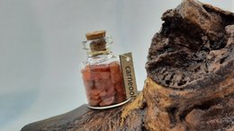 Carnelian glass bottle with cork stopper, featuring a reddish-orange color and irregular, natural shape.