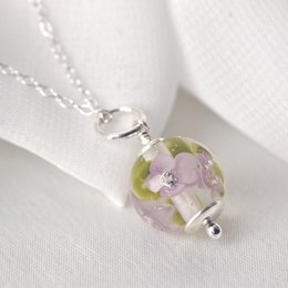 Delicate necklace with lilac glass flowers. Features a round glass pendant with floral accents in shades of purple and green. Elegant and feminine design.