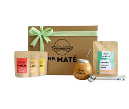 A gift box containing a Yerba Mate starter set, including the original 150g Yerba Mate tea, a traditional gourd, and a metal straw. The set is presented in a brown gift box with a green bow.