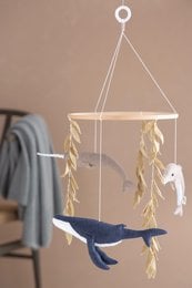 Hanging mobile with wooden ocean-themed shapes including a whale and fish, suspended from a wooden frame with feathers.