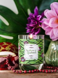 A round, tall green candle with a floral label, surrounded by pink flowers and red beads.