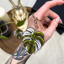 Monstera leaf-shaped keychain in green and white colors, featuring a tropical leaf design.