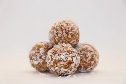 A group of round, brown energy balls coated in shredded coconut. The energy balls appear to be made from a mixture of nuts, seeds, and dried fruit, providing a nutritious and energy-boosting snack.