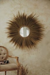 Round, natural-looking mirror with a starburst frame made of brown feathers. Available in natural, beige, bronze, and magenta color variants.