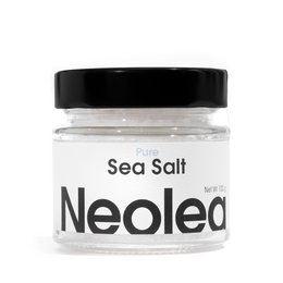 Neolea Sea Salt Pure - NEW DESIGN. Natural sea salt in a glass jar with a black lid. The salt is displayed on a picnic blanket with various food items.