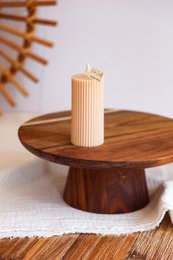  A tall, cylindrical pink candle standing on a round wooden pedestal.