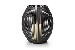 Tall, cylindrical black lantern with vertical slats creating a striped pattern. Made of metal with a warm, ambient glow from the light inside.