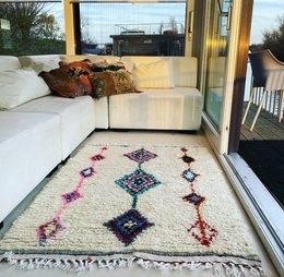 Handwoven Moroccan-style area rug with vibrant diamond pattern in shades of pink, blue, and white.