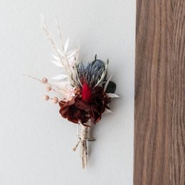 Burgundy and green floral boutonniere with dried flowers, eucalyptus, and feathers.