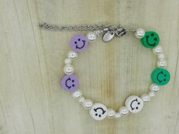 A colorful kids' bracelet with smiley face charms, pearls, and green accents. The bracelet has a playful, whimsical style.