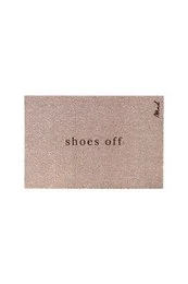 Rectangular pink doormat with the text "shoes off" printed on it. The doormat is placed on a white floor with a pair of blue shoes next to it.